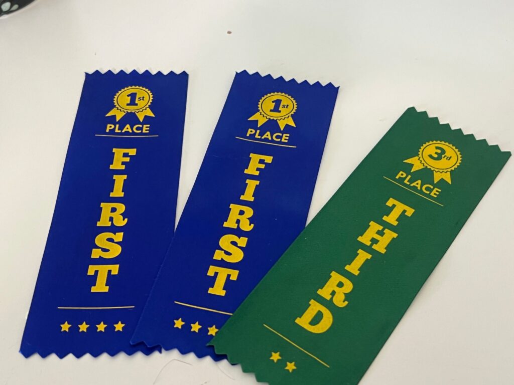 Three swimming carnival ribbons: two blue first-place ribbons and a green third-place ribbon.